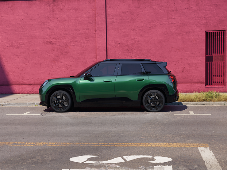 Side view of the all-electric MINI Aceman in British Racing Green and Black Roof, on a street.