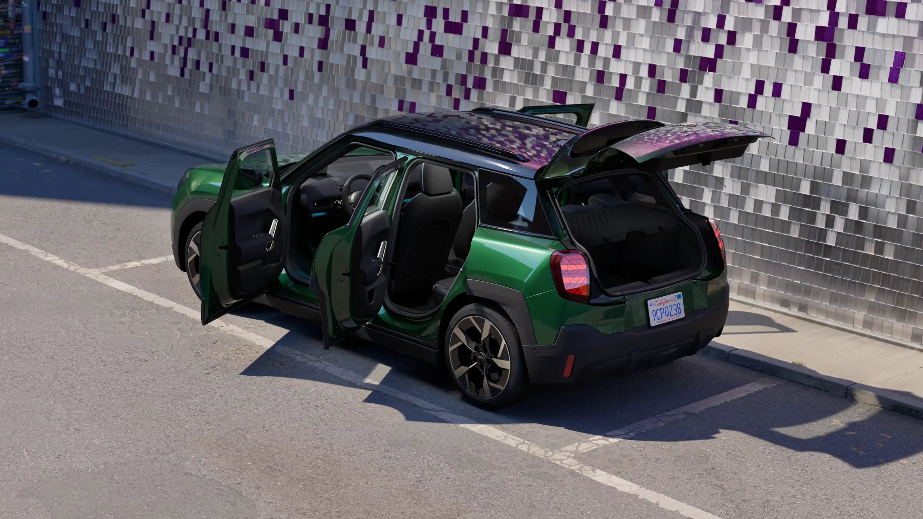 Rear side view of parked all-electric MINI Aceman in British Racing Green in car park with all doors open and coloured wall in the background