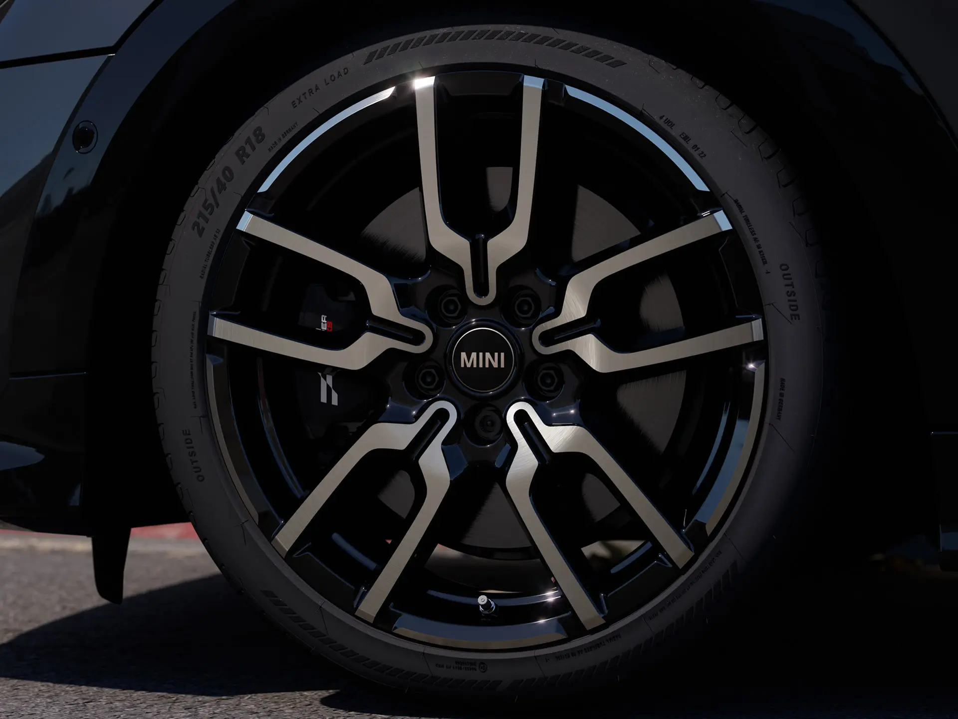 Close-up of the JCW Lap Spoke alloy wheel, showing its distinctive open spoke design in a Jet Black finish. 