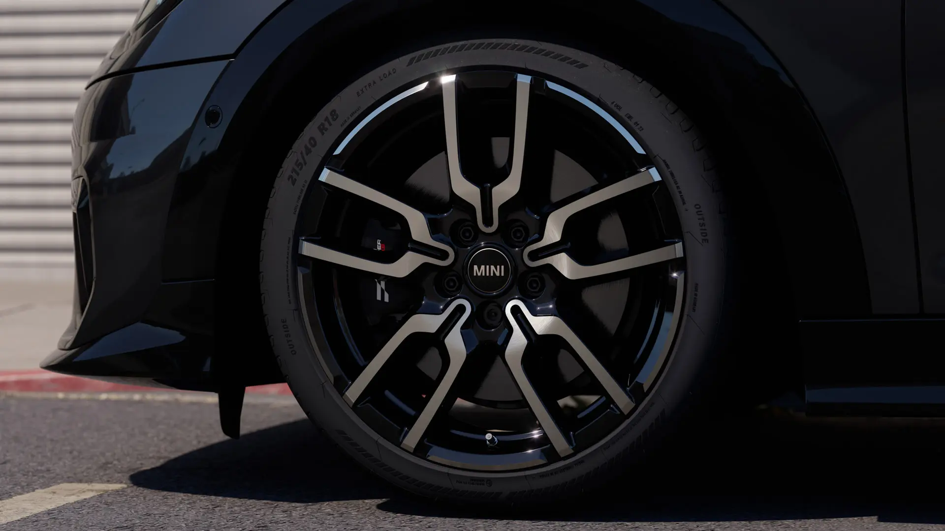 Close-up of the JCW Lap Spoke alloy wheel, showing its distinctive open spoke design in a Jet Black finish. 