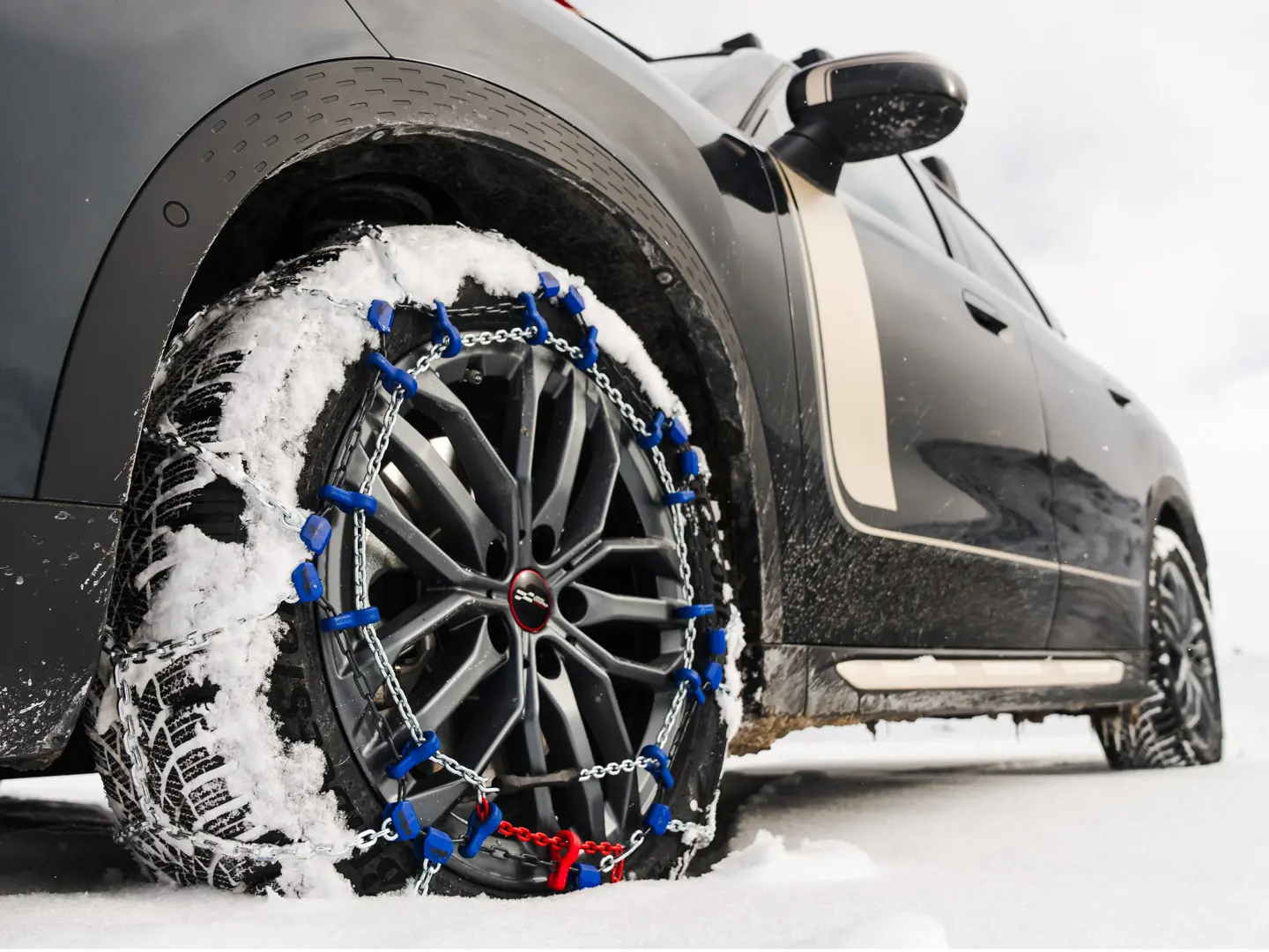 Close-up of a tyre chain installed on the wheel of a MINI Countryman for extra traction as it drives through heavy snow. 