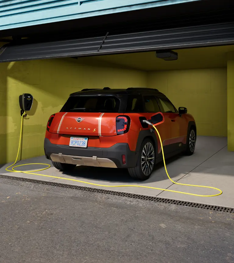 All-electric MINI Aceman S being charged with MINI Wallbox Plus, rear view, parked in garage.