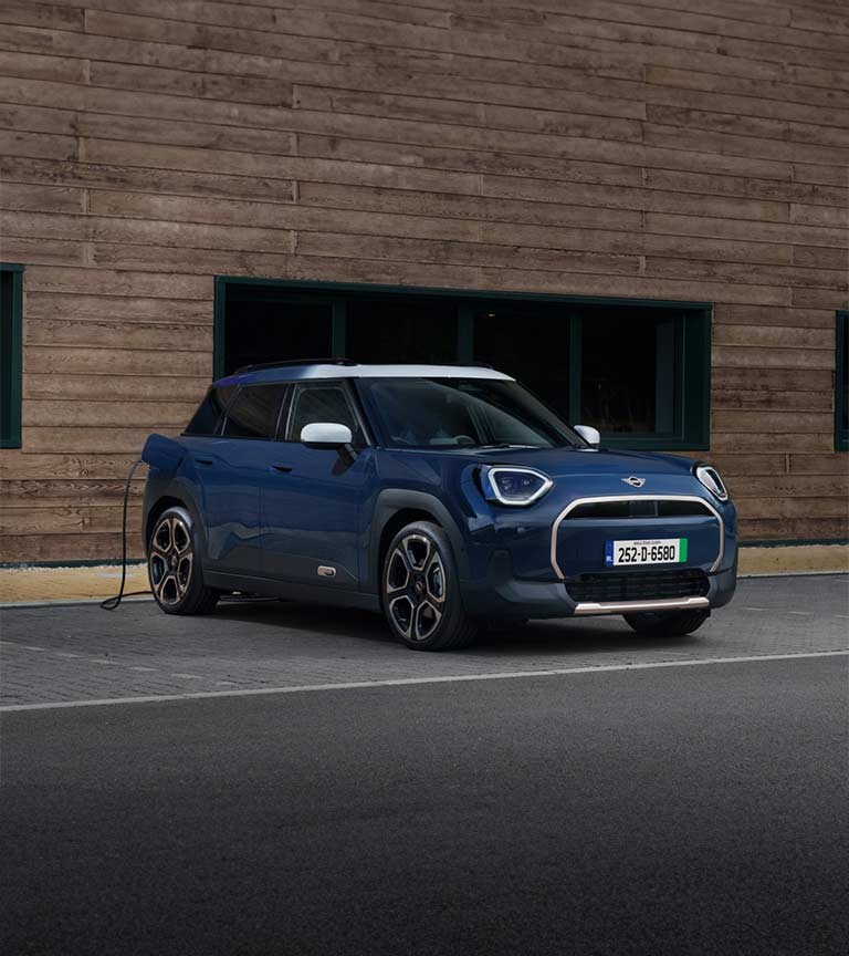 A blue Mini Aceman parked at an EV charging point, connected by a charging cable on the driver’s side.