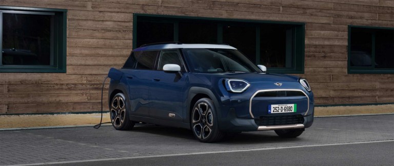 A blue Mini Aceman parked at an EV charging point, connected by a charging cable on the driver’s side.
