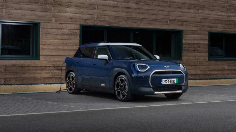 A blue Mini Aceman parked at an EV charging point, connected by a charging cable on the driver’s side.