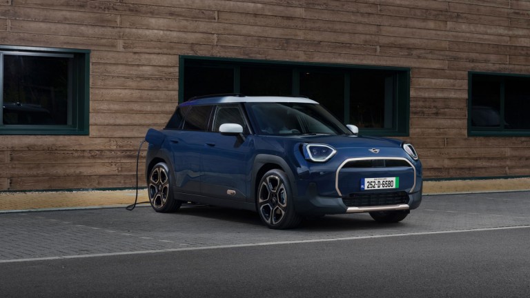 A yellow MINI Cooper car parked on a cobblestone street beside brick buildings.