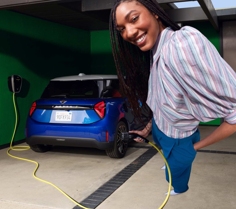 Woman holding charger cable, all-electric MINI Cooper in garage