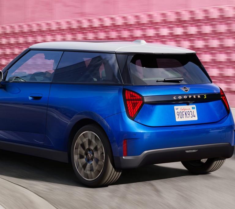 all-electric MINI Cooper side and rear driving in front of pink wall